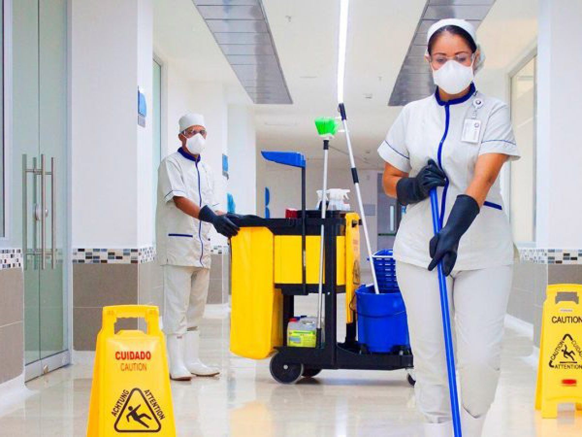 Personal de limpieza con fregona y carrito de limpieza en un luminoso pasillo de hospital