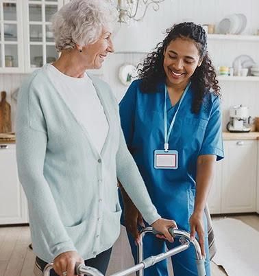 Cuidador ayudando a un adulto mayor a caminar con un andador en una luminosa cocina.