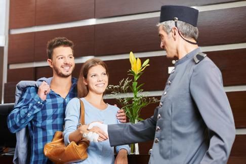 Una pareja de viajeros sonríe mientras una recepcionista del hotel, vestida con uniforme gris