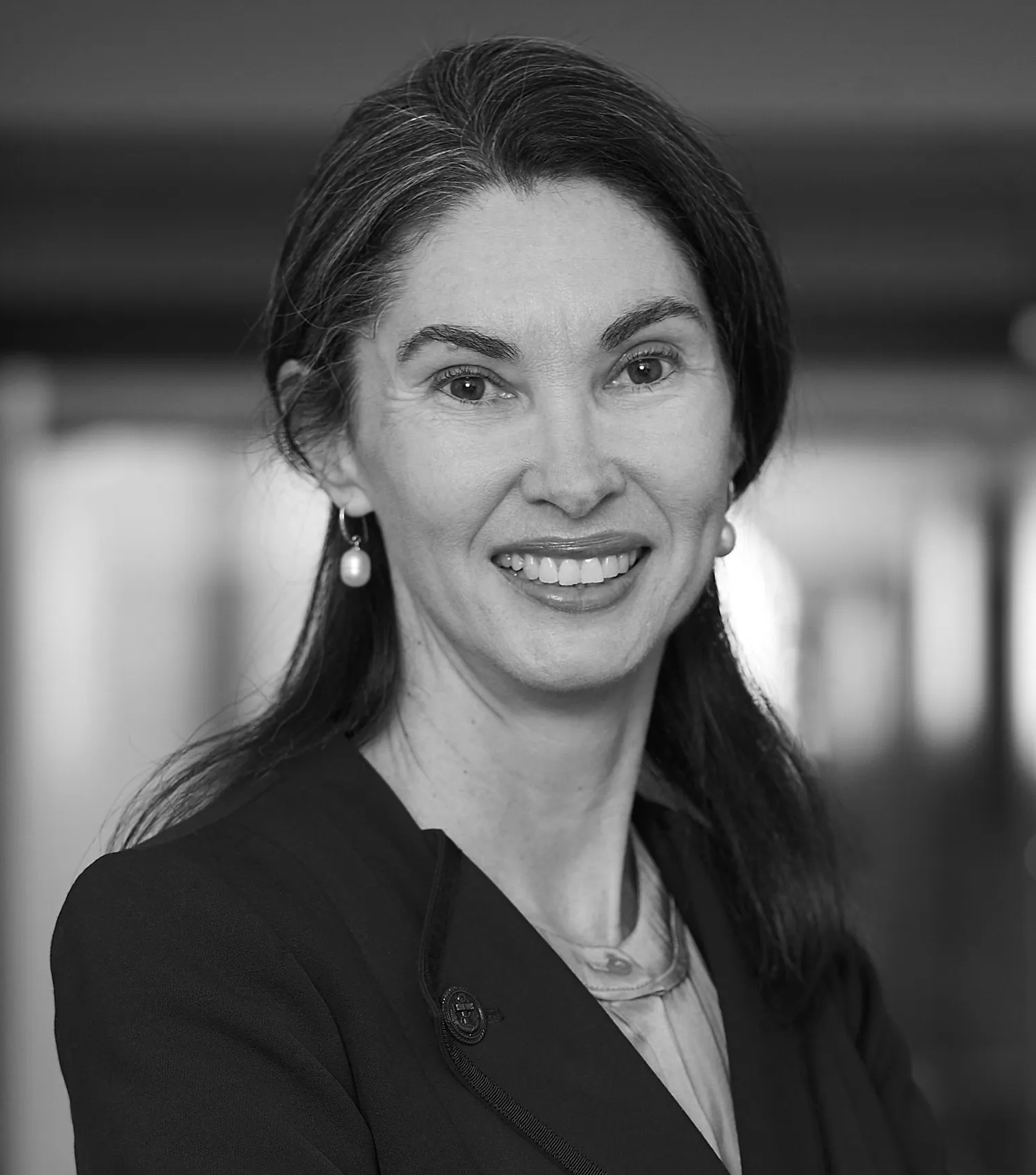 A woman in a suit and earrings is smiling in a black and white photo.