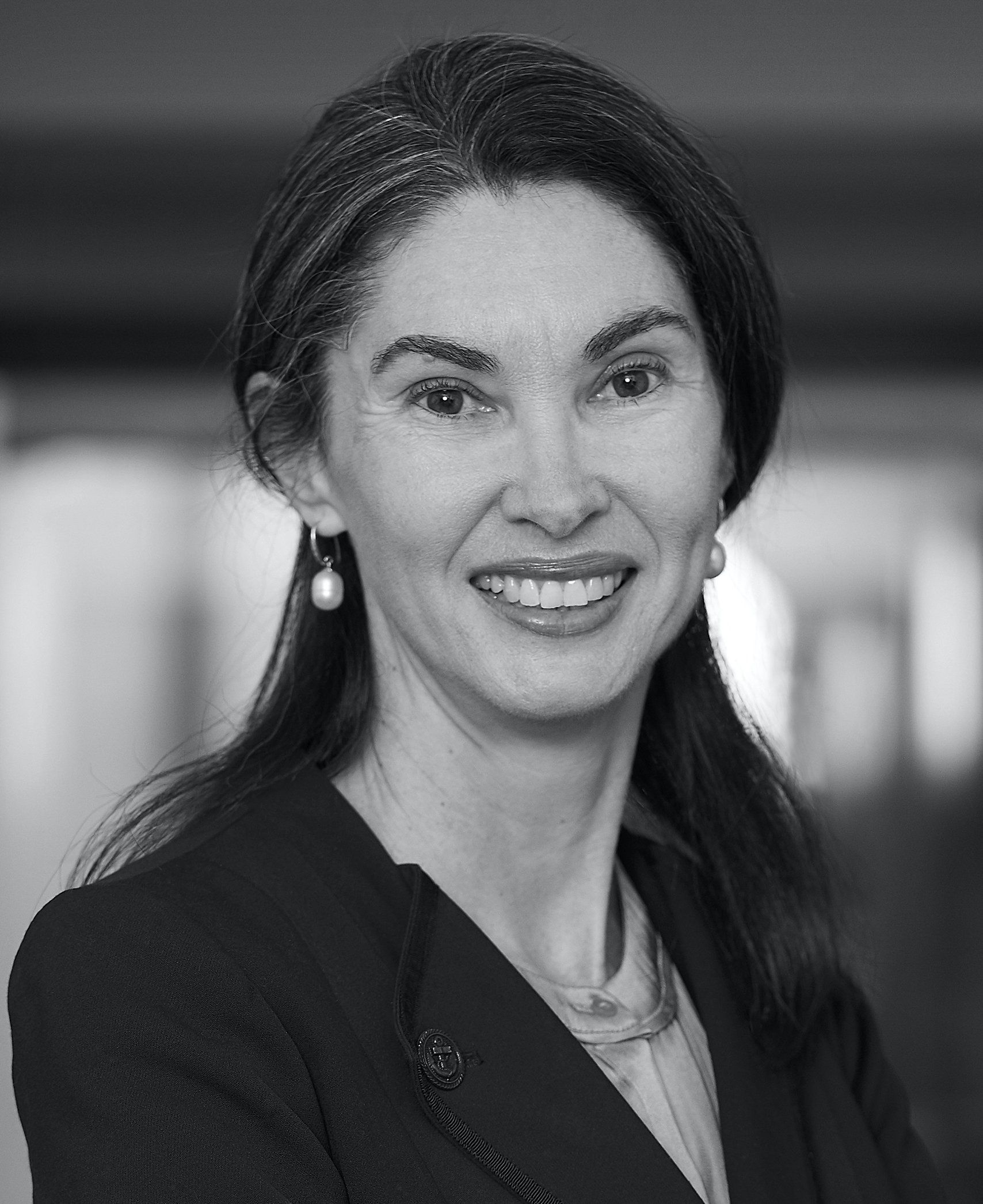 A black and white photo of a woman in a suit and earrings smiling.
