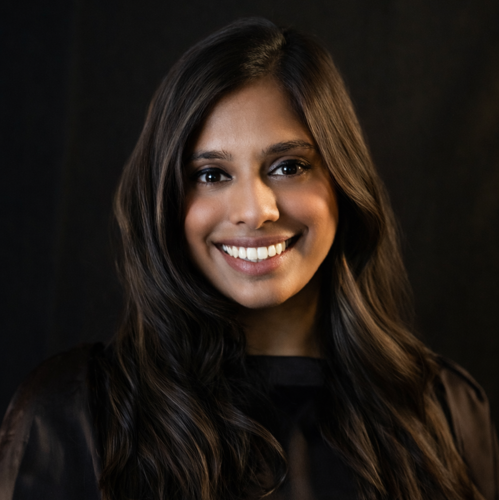 Woman with long, wavy brown hair smiles at the camera against a dark backdrop.