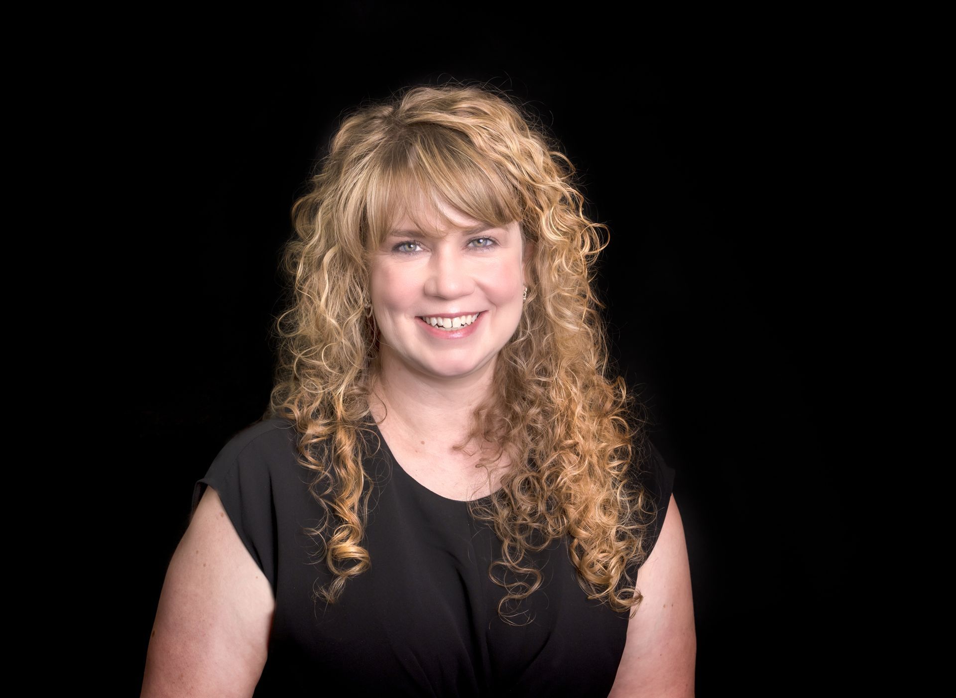 A woman wearing a pearl necklace is sitting in front of a bookshelf.