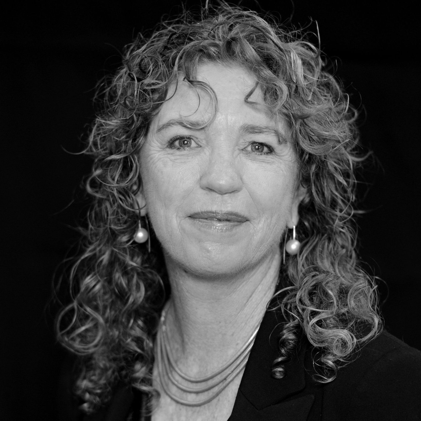 A black and white photo of a woman with curly hair and pearl earrings.