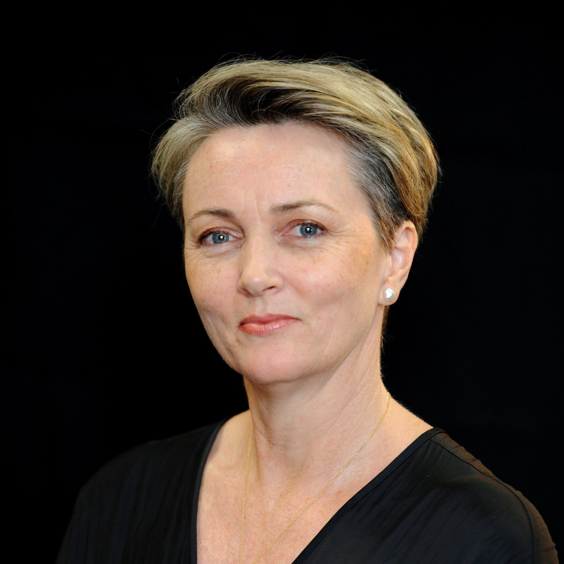 A woman with short blonde hair is wearing a black shirt and earrings.