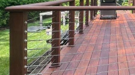 A wooden deck with a stainless steel railing and a grill.