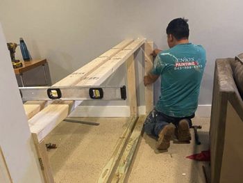 A man is kneeling down in a living room while working on a piece of wood.