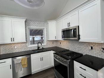 A kitchen with white cabinets , black counter tops , stainless steel appliances and a window.
