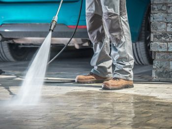 A man is using a high pressure washer to clean a driveway.