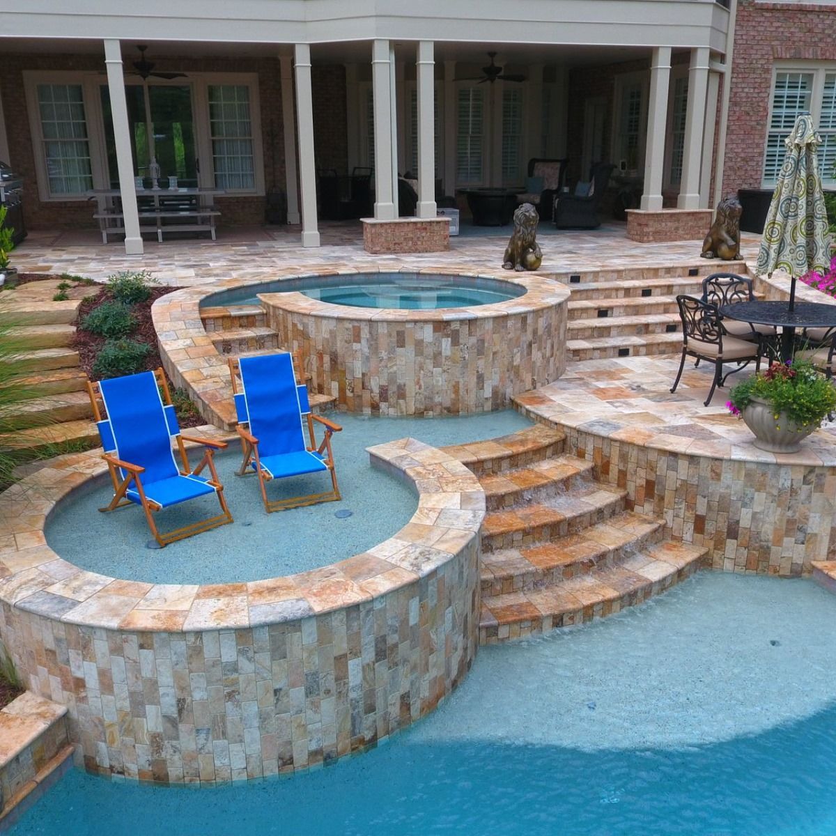 Swimming pool with a hot tub, lounge chairs, and patio; brick home in the background.
