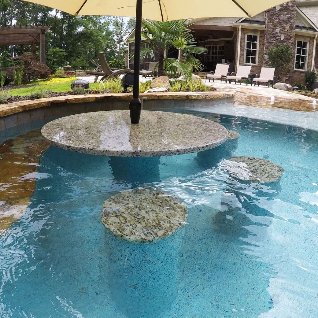 Pool with swim-up bar; a large table with umbrella and floating stone seats.