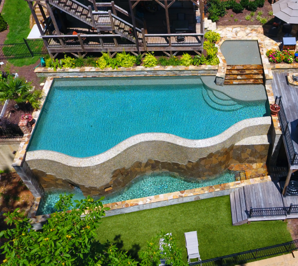 Aerial view of a luxury swimming pool with a stone wall feature and wooden deck.