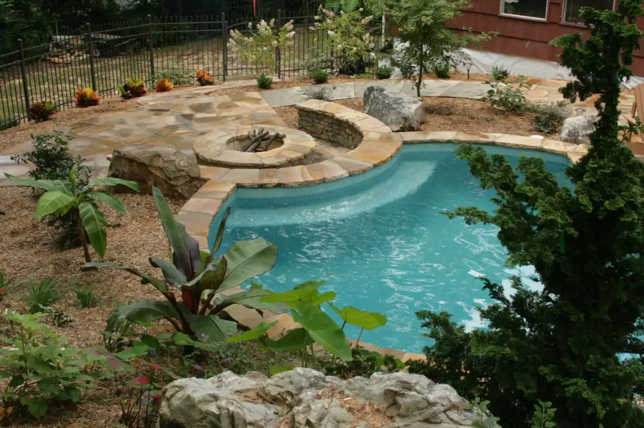 Swimming pool with built-in fire pit and steps, surrounded by landscaping and boulders.