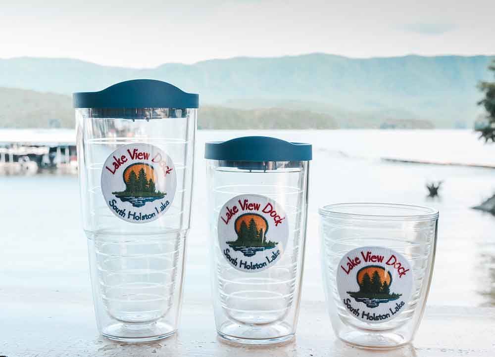 Three glasses are sitting on a table in front of a lake.