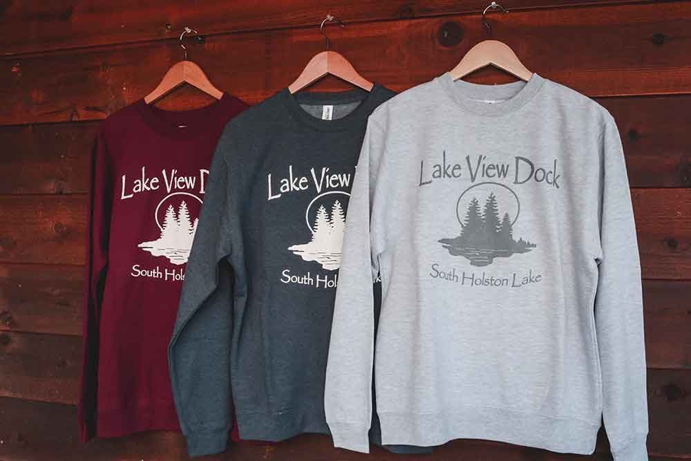 Three lake view dad sweatshirts are hanging on a wooden wall.