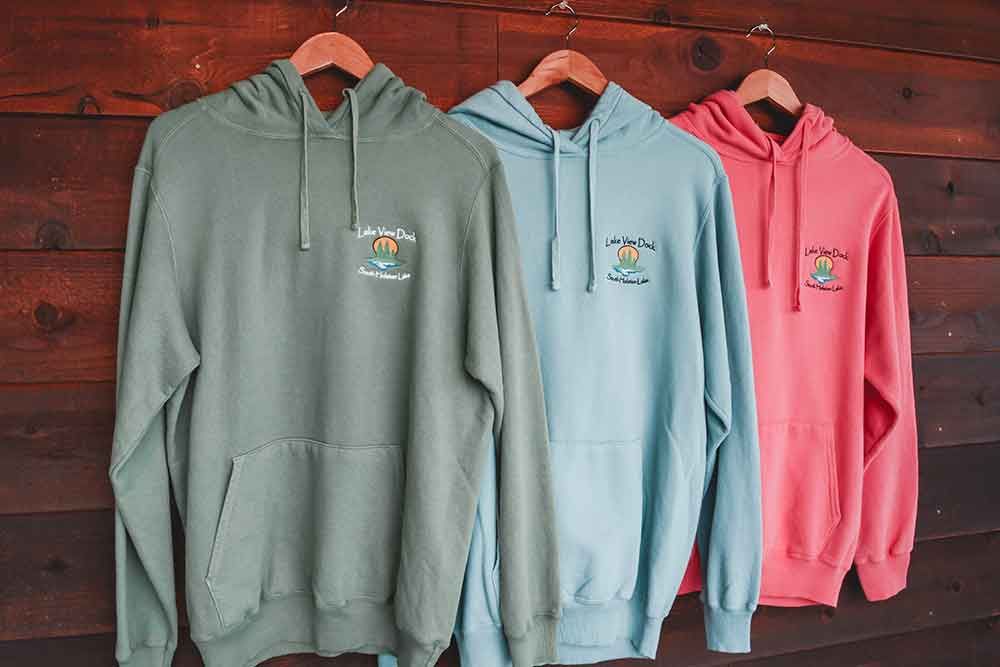 Three hoodies are hanging on a wooden wall.