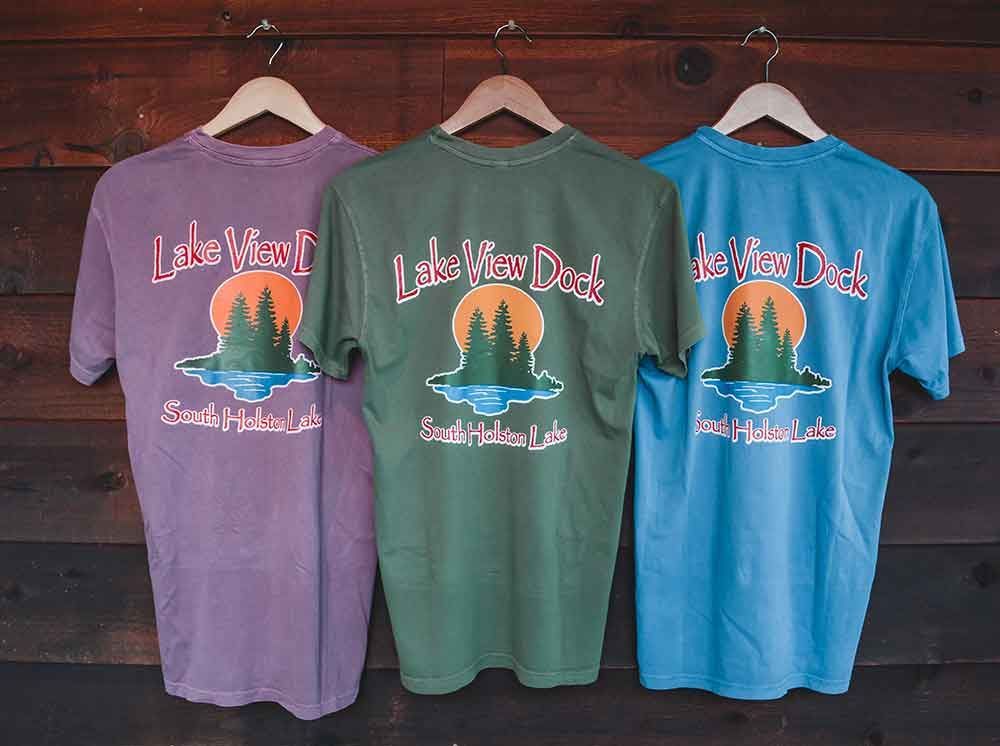 Three t-shirts are hanging on a wooden wall.