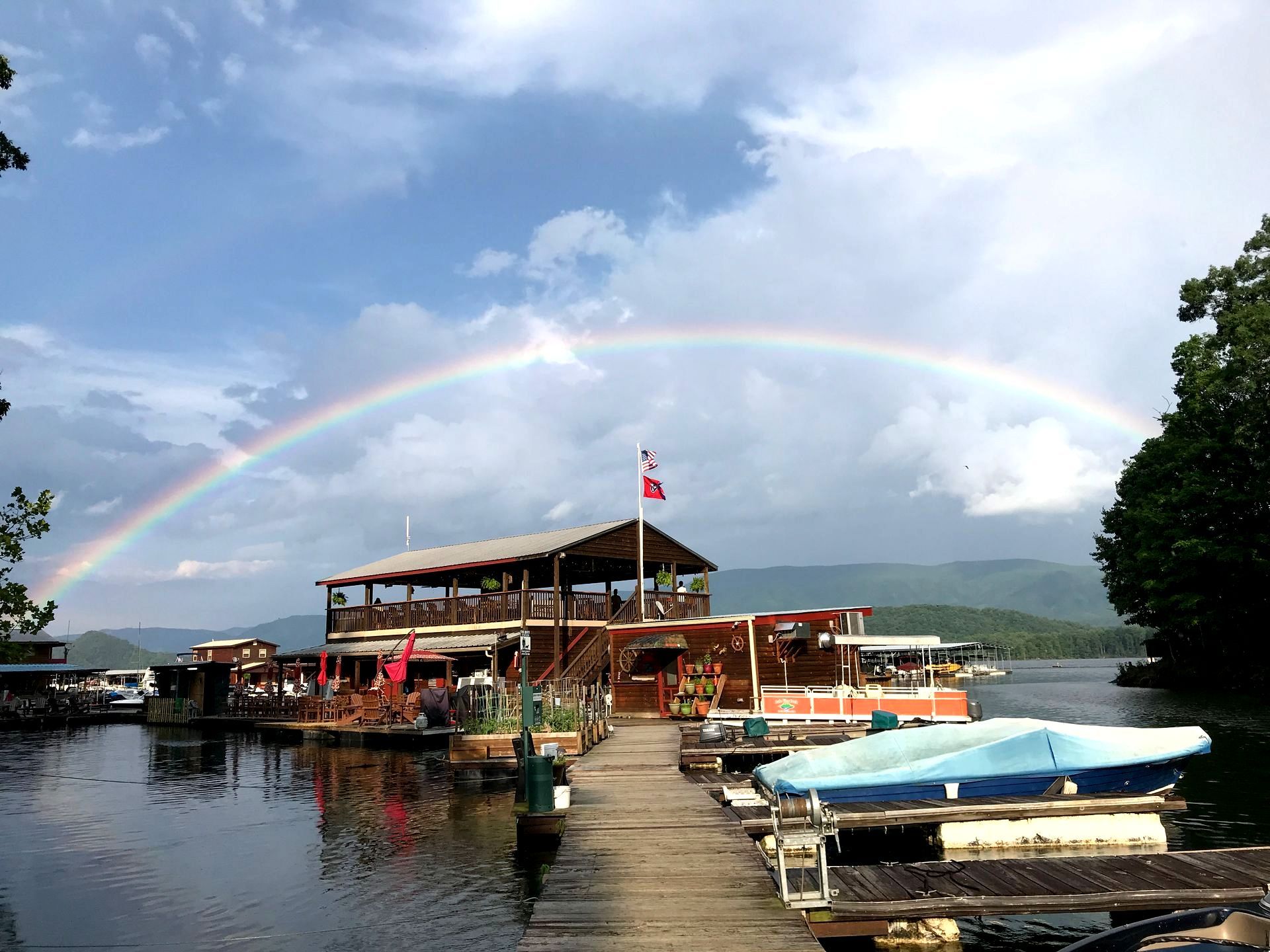 A rainbow is visible over a dock with boats docked in the water.