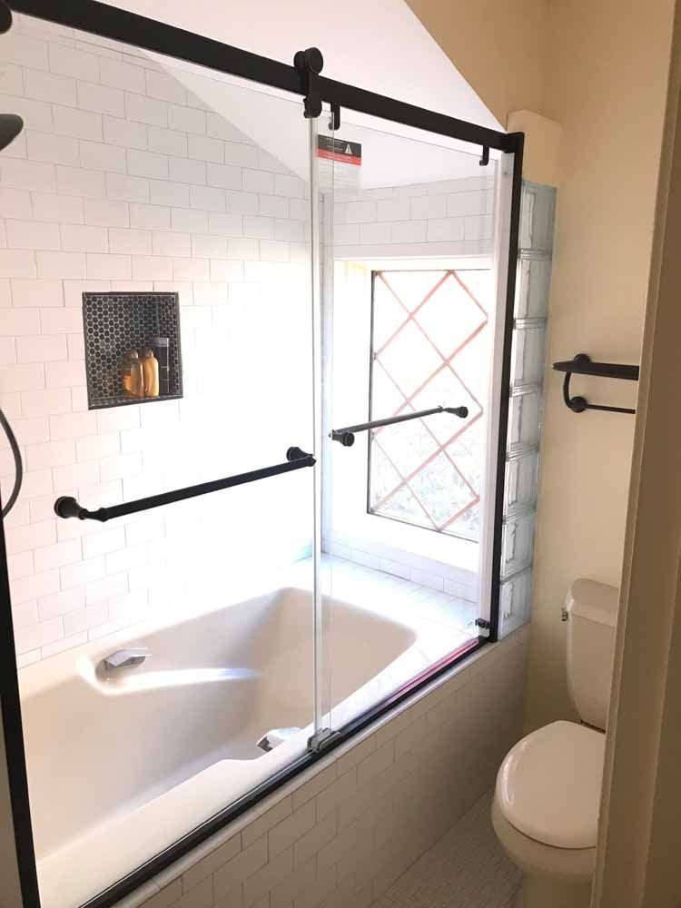 A bathroom with a tub , toilet and shower with a sliding glass door.