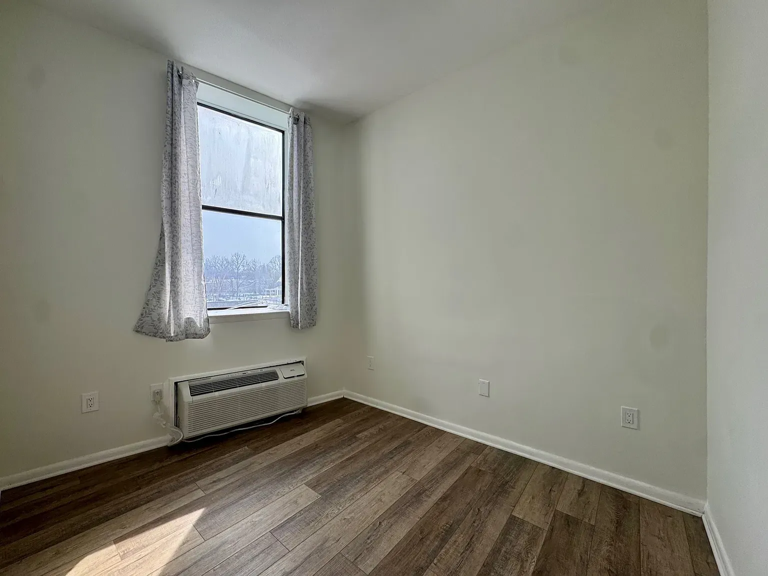 Empty room with a window, white walls, radiator, and wood-look flooring