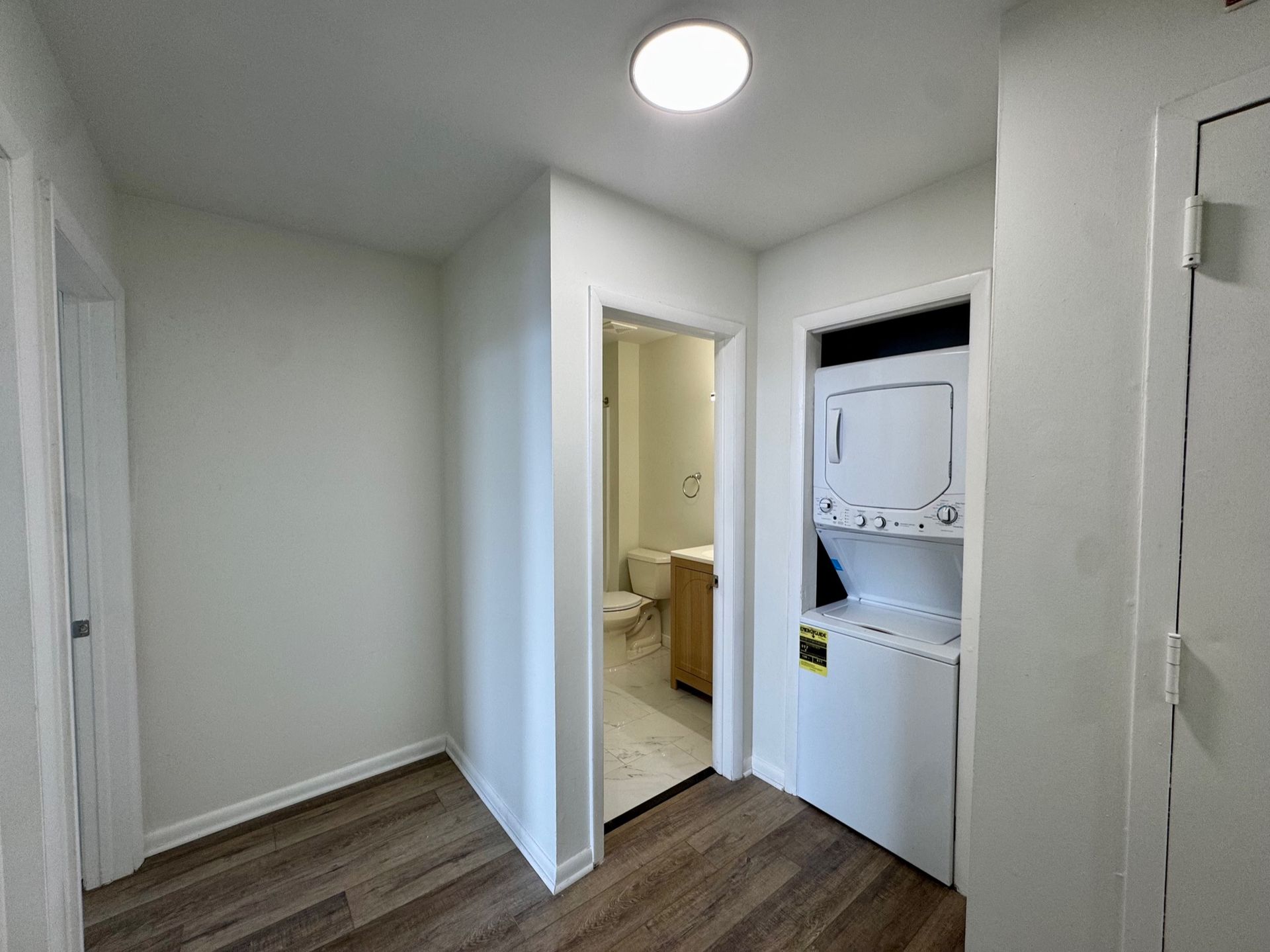 Small hallway with wood floors, white walls, ceiling light, and an open door to a bathroom.