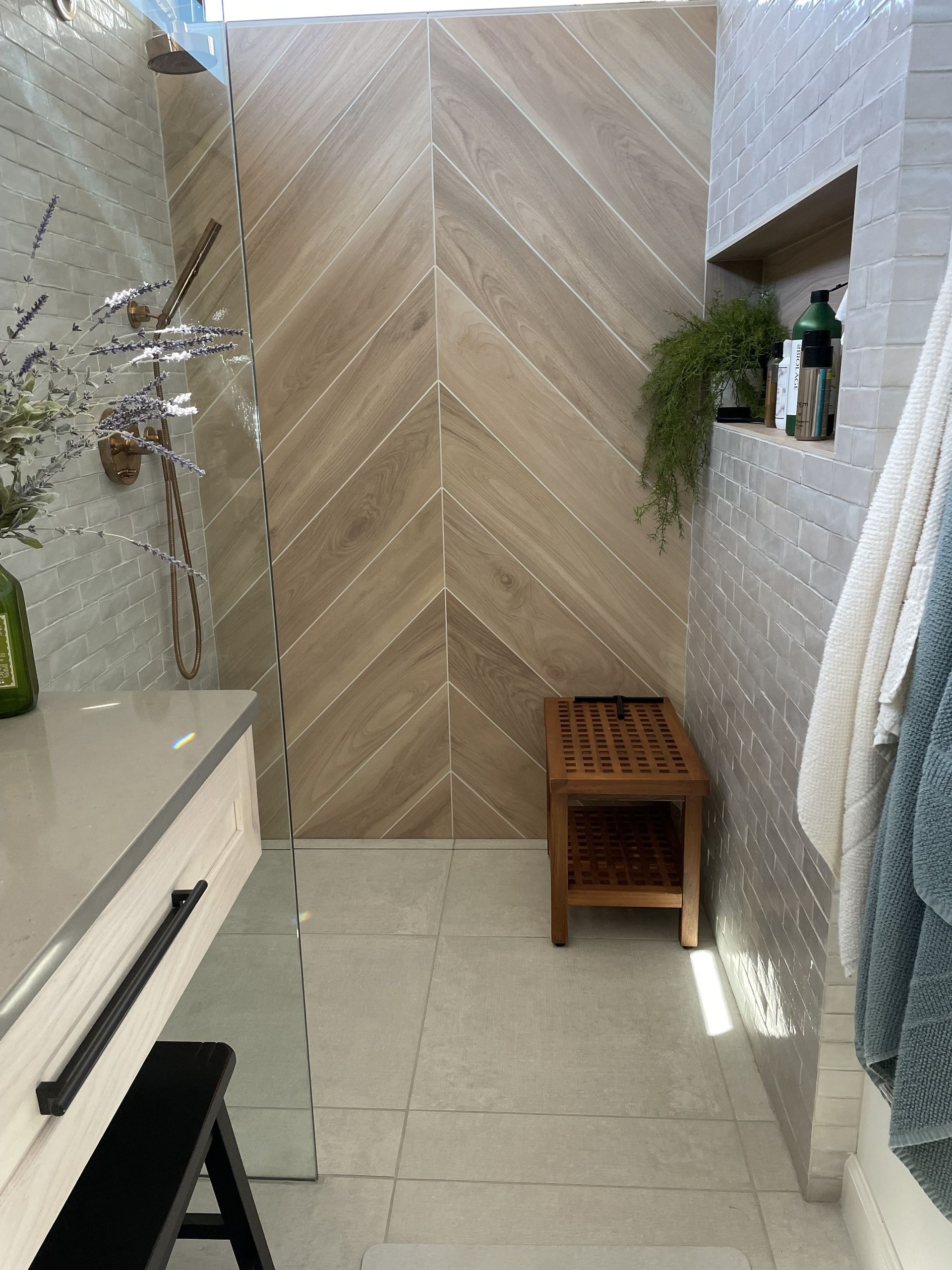 Bathroom with wood-look accent wall, shower bench, and towel rack. Neutral tones with natural light.