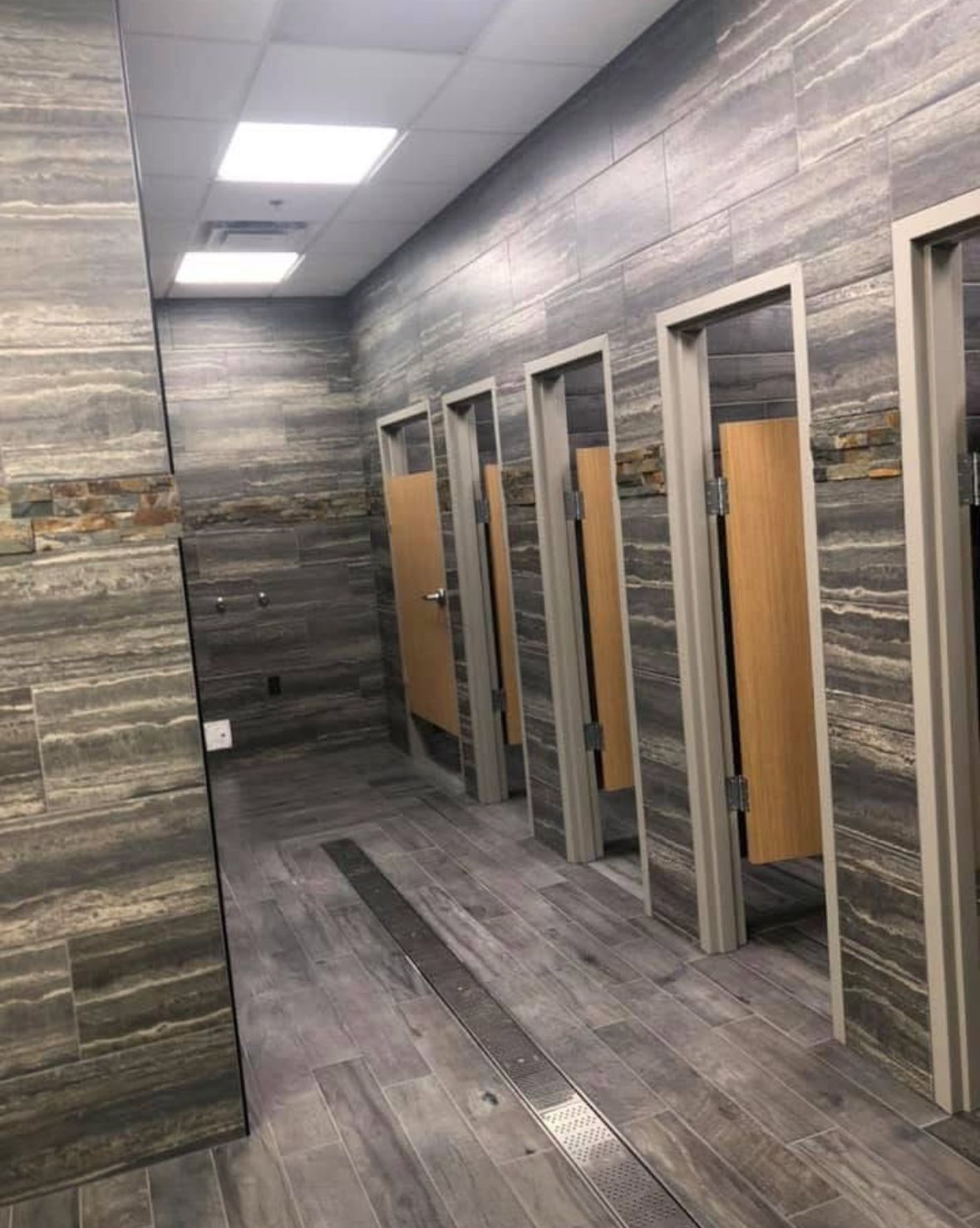 Public restroom with grey stone-like walls and wooden stall doors.