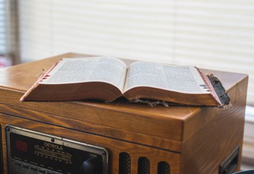 An open bible is sitting on top of a wooden record player.