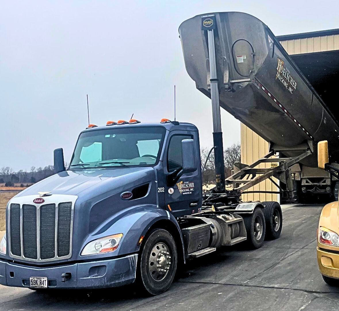 Blue semi-truck with trailer dumping contents into a building.