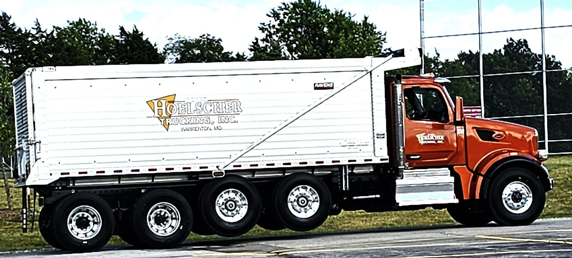 Orange and white dump truck with a white trailer, parked outdoors.