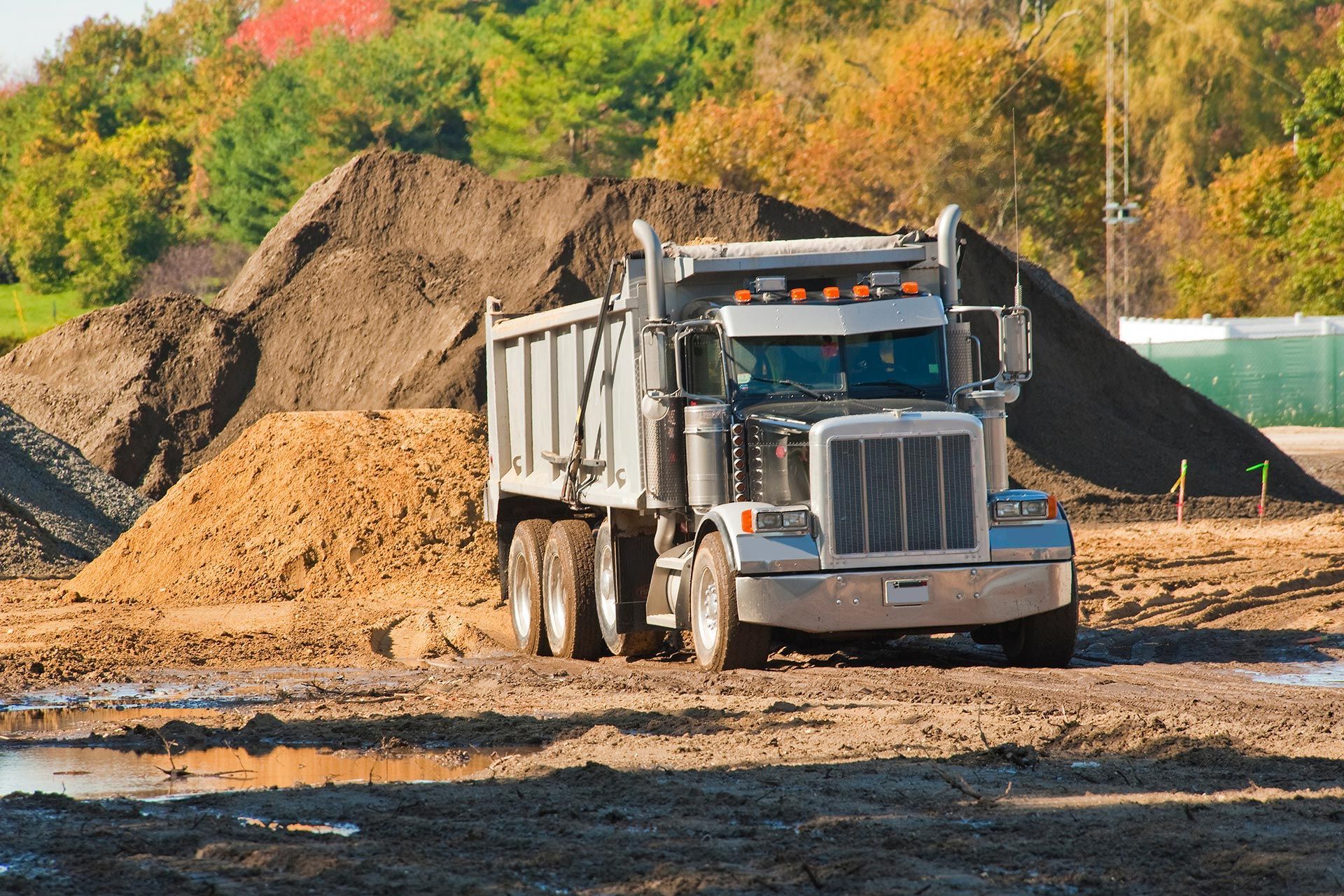 Heavy dump truck parked at a construction site with large piles of dirt in the background. Heavy dump truck parked at a construction site with large piles of dirt in the background.
