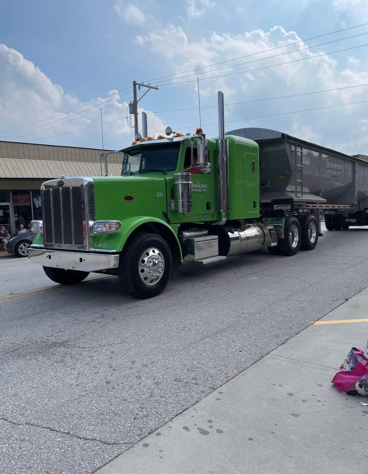 Green semi-truck hauling a trailer on a paved road under a partly cloudy sky.