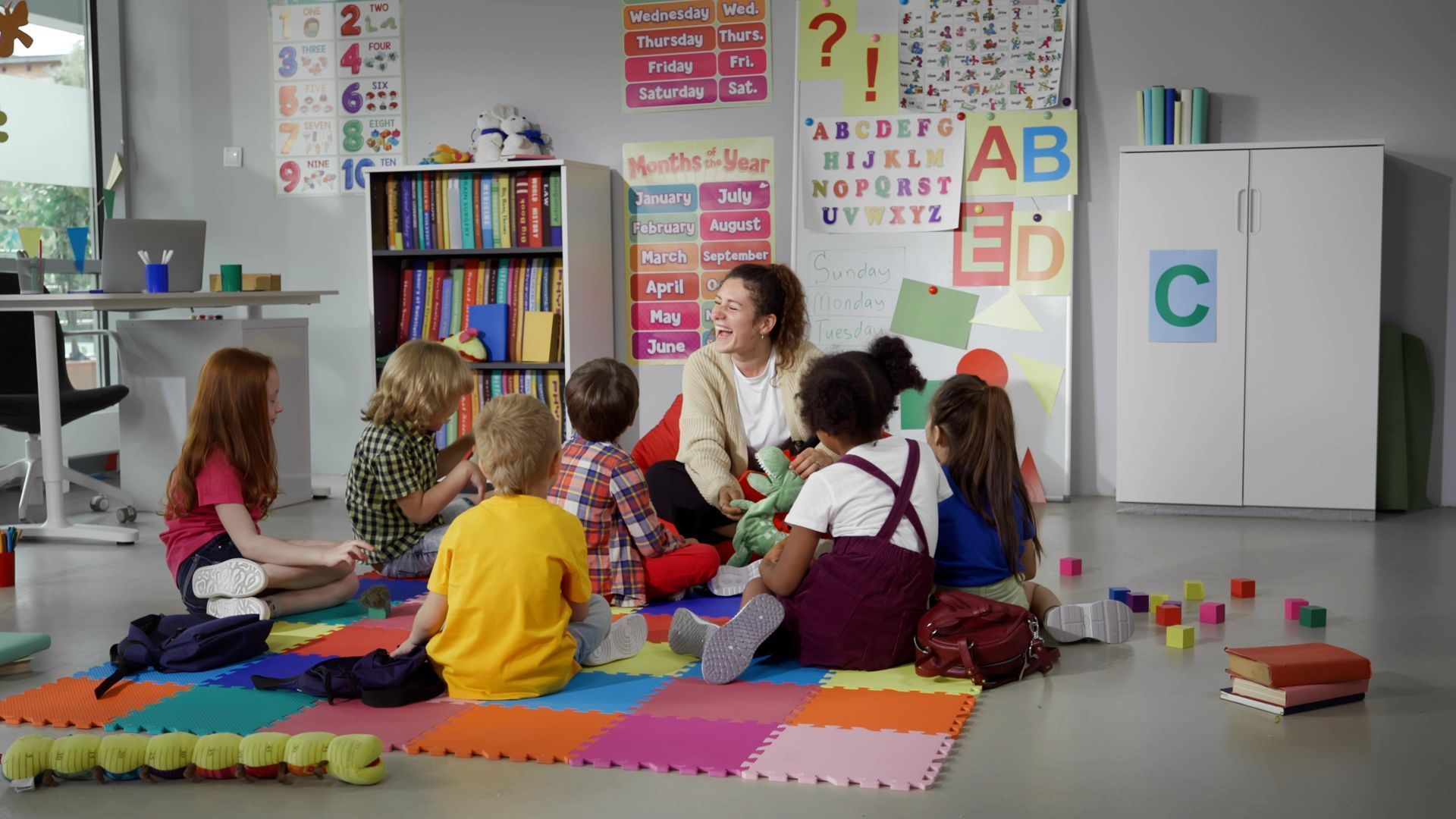A group of children are sitting on the floor in a classroom with a teacher.