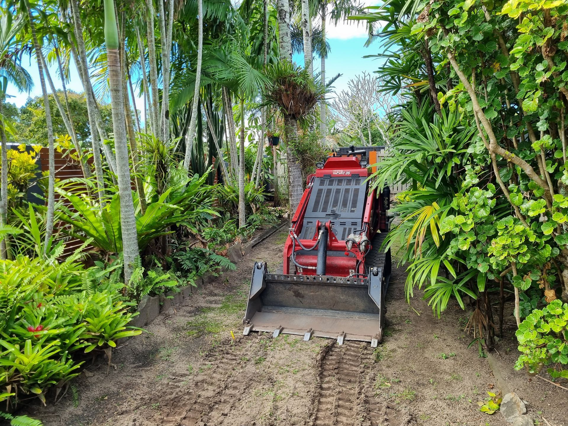 A loader is driving down a dirt road surrounded by trees.