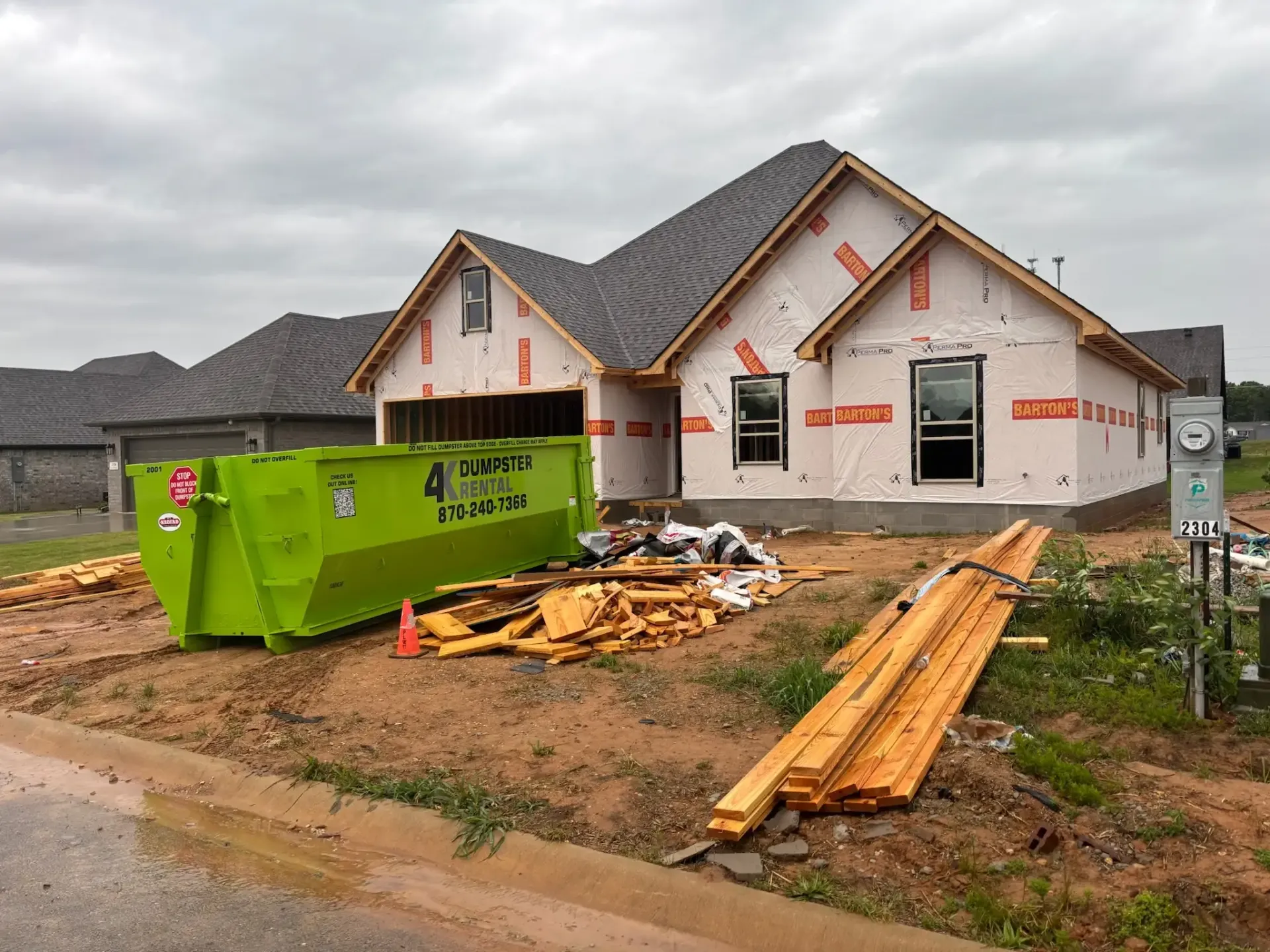 A green dumpster is sitting in front of a house under construction.