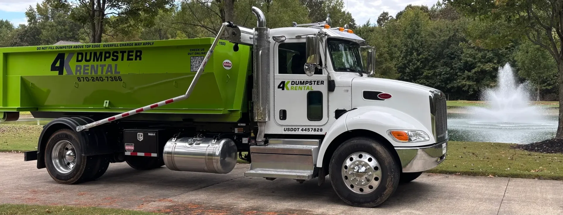 A dumpster is being pulled by a truck on a trailer.