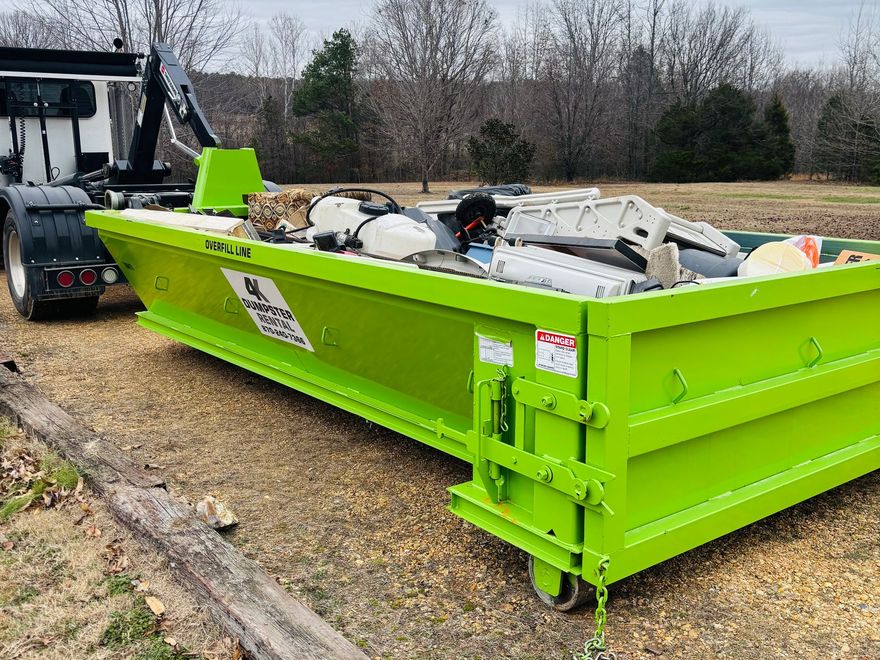 A green dumpster is sitting on top of a gravel road.