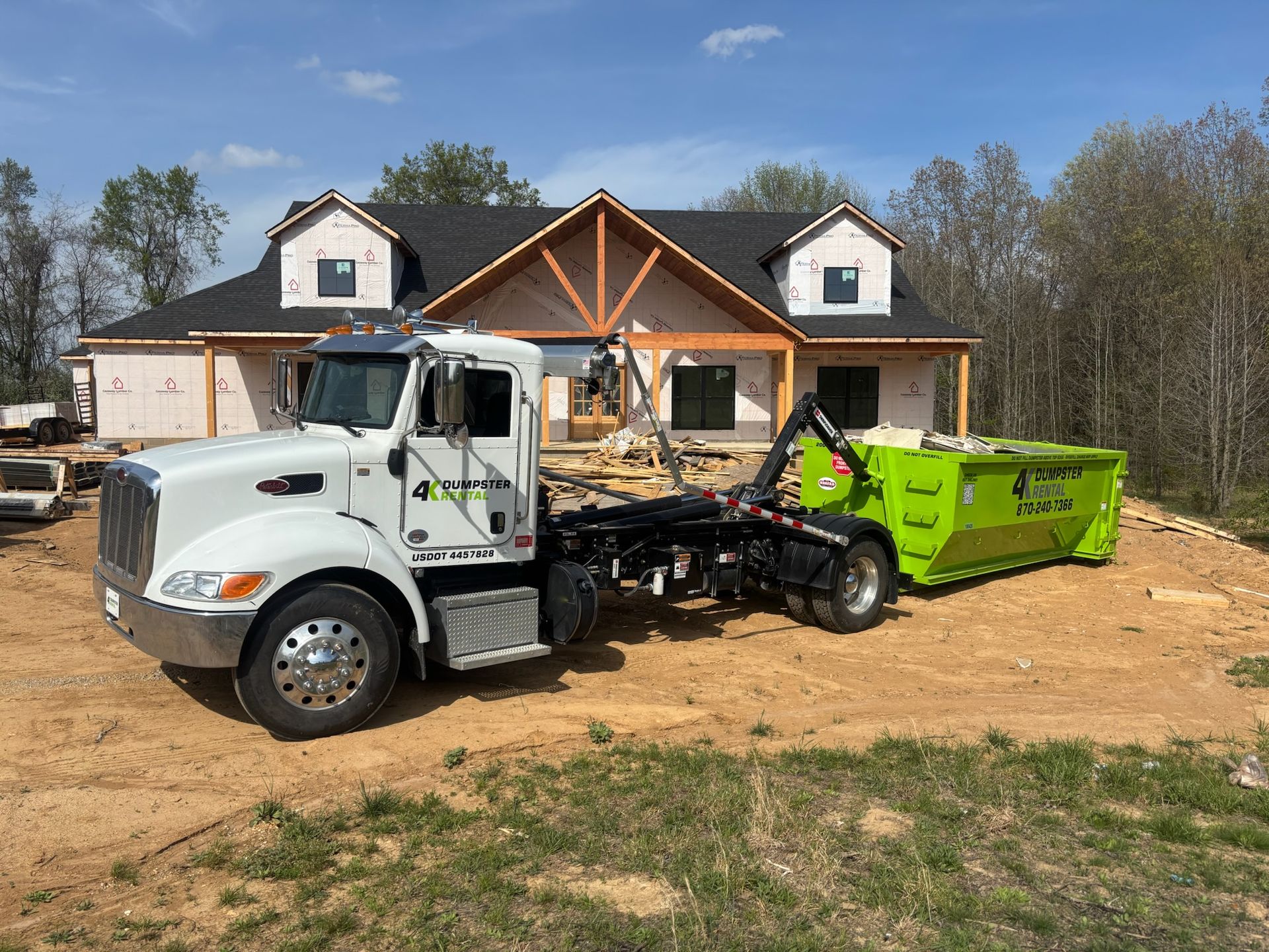 A green dumpster is sitting in front of a house under construction.