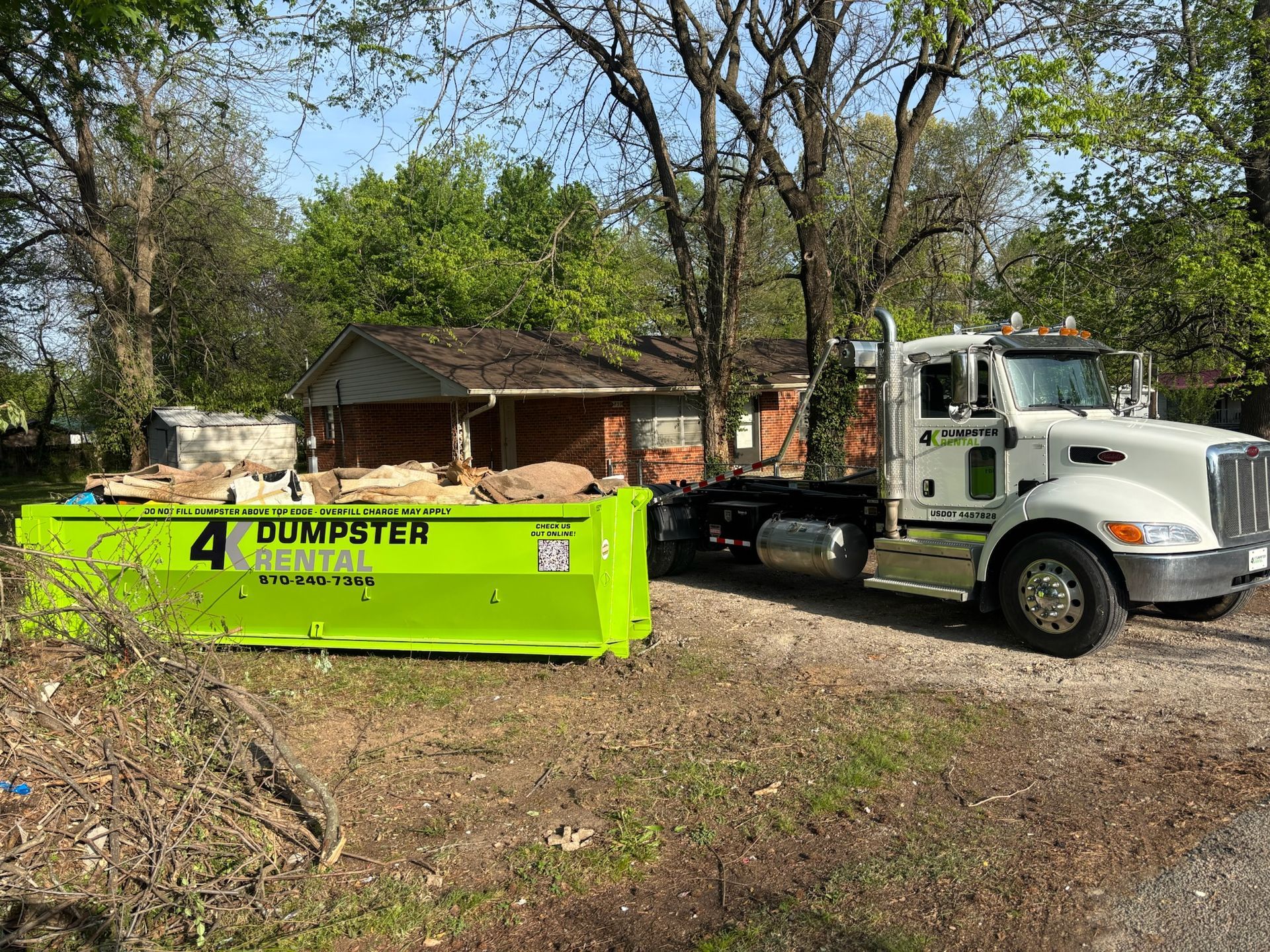 A green dumpster is parked in front of a house.