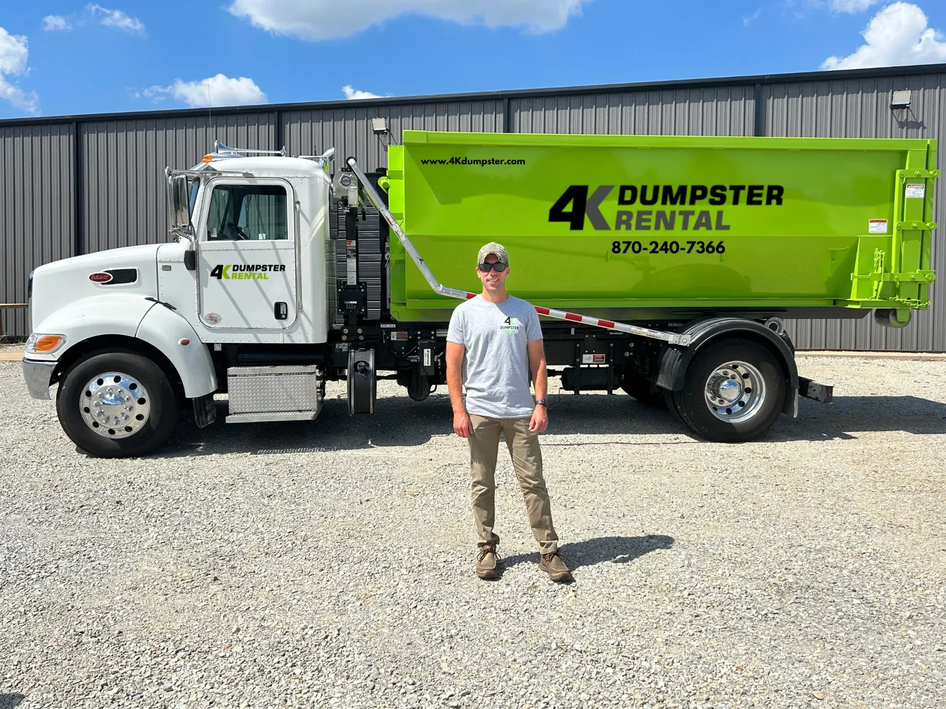 A green dumpster is sitting on top of a gravel road.