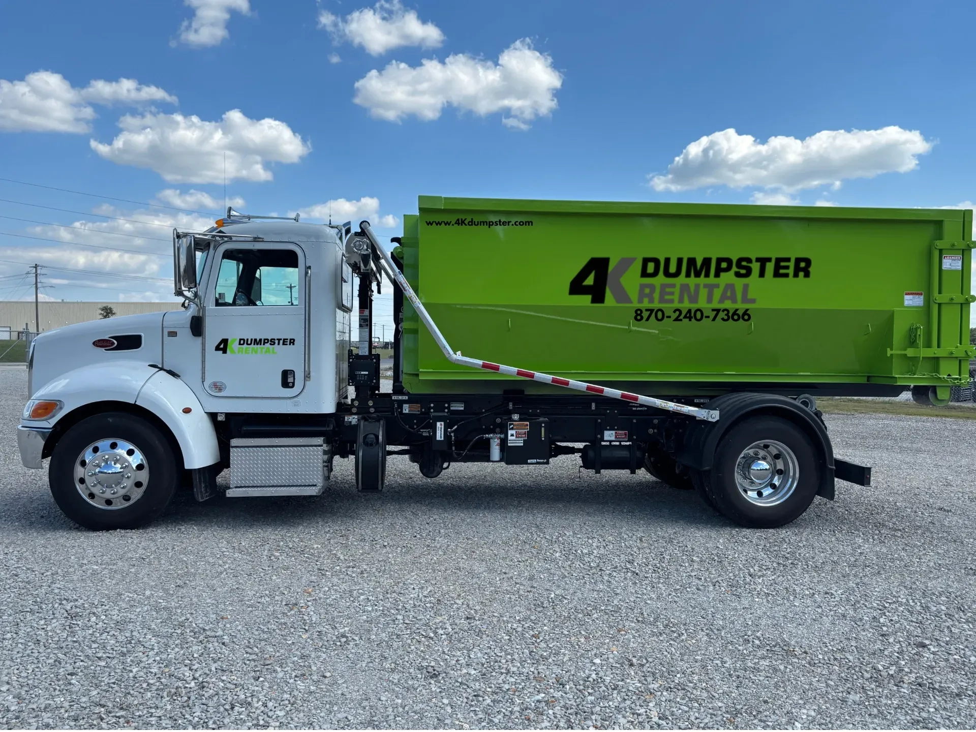 A dumpster is sitting in a gravel lot next to a truck.