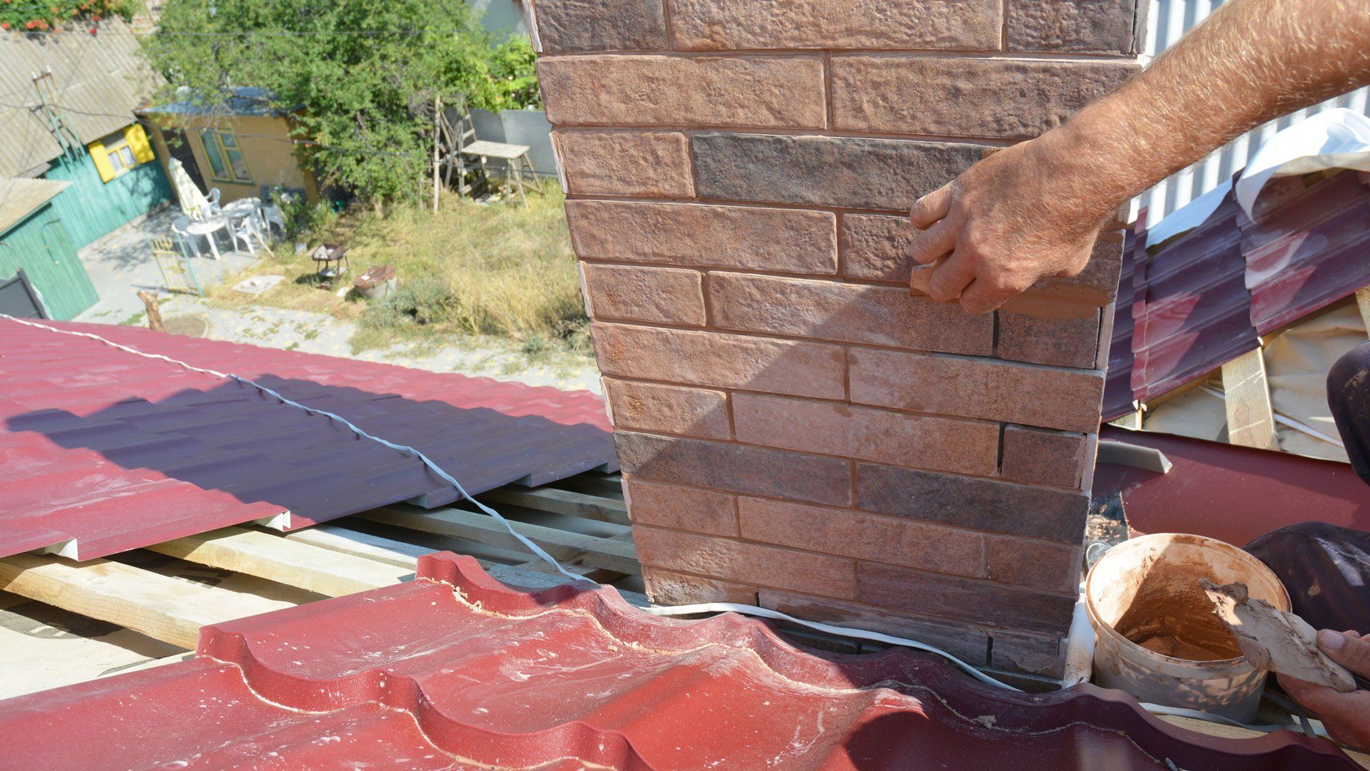 Man applying brick veneer to a chimney on a red metal roof.