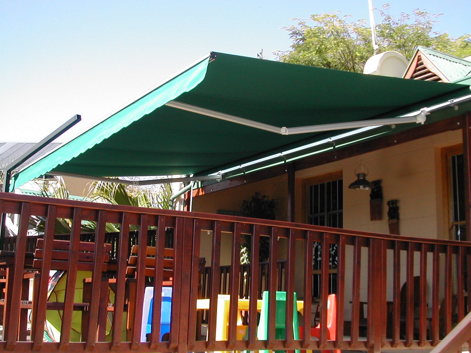 A green foldable awning over a wooden deck fitted by Blind & Shutter City in Menlo Park, Pretoria.