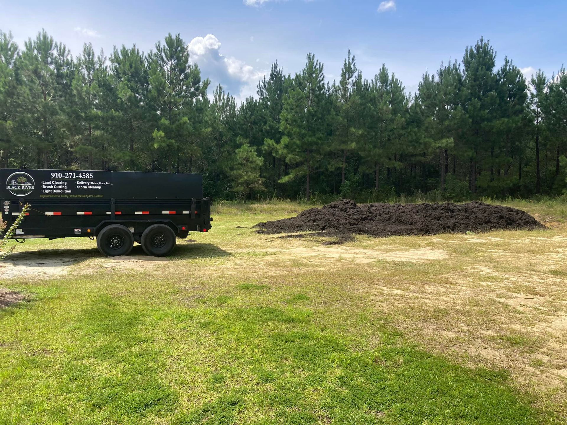 A dump truck is parked in a grassy field next to a pile of dirt.