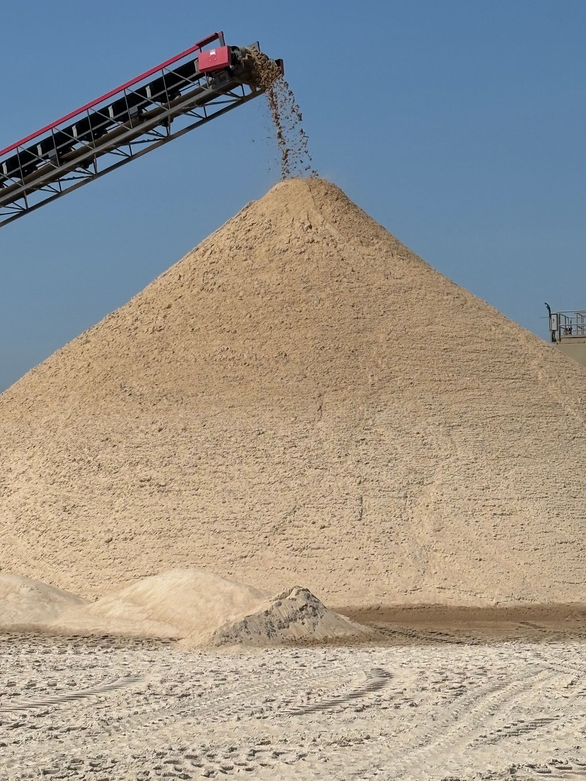 A conveyor belt is pouring sand into a large pile