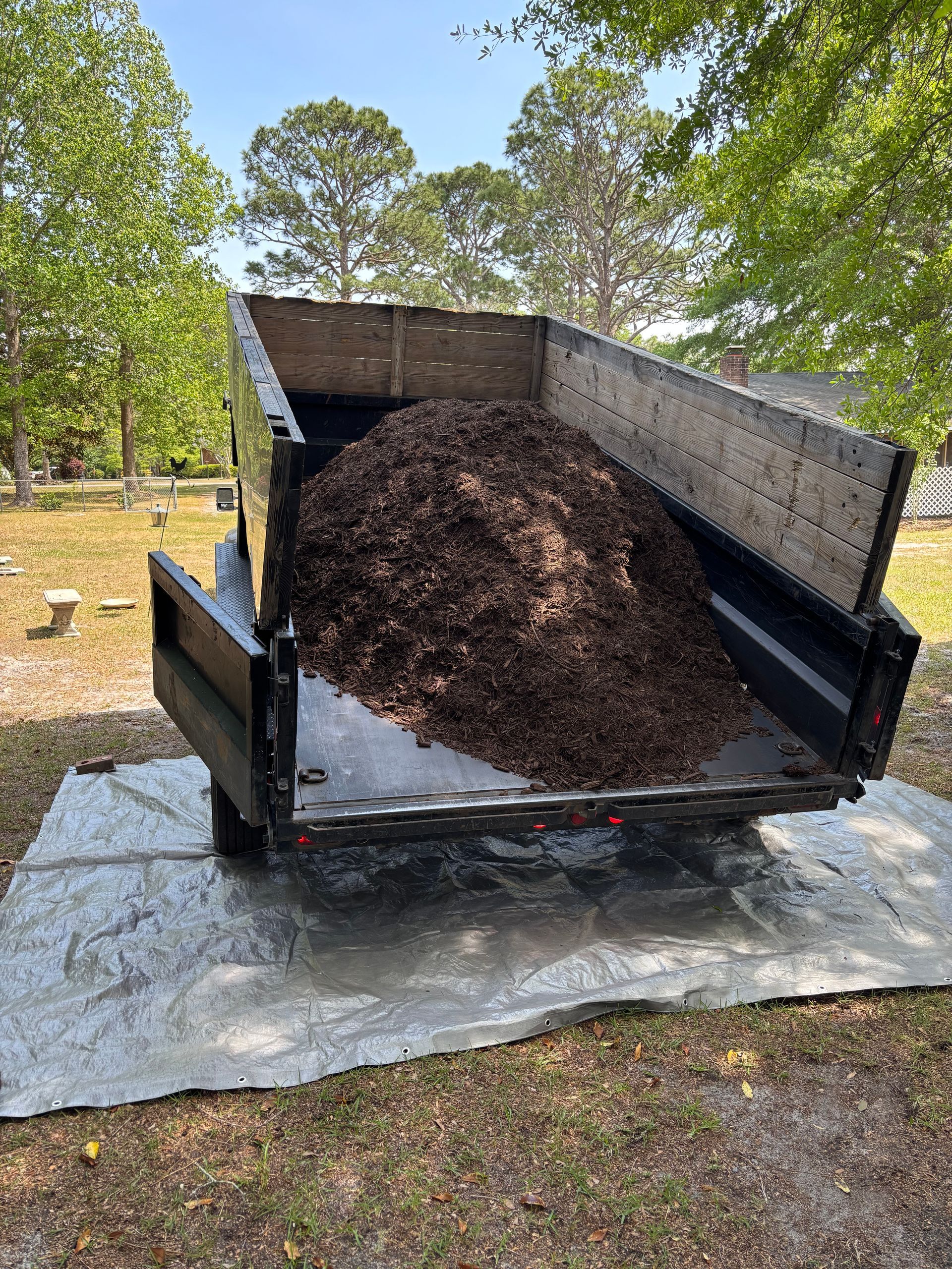 A dumpster filled with dirt is sitting on top of a tarp on the ground.