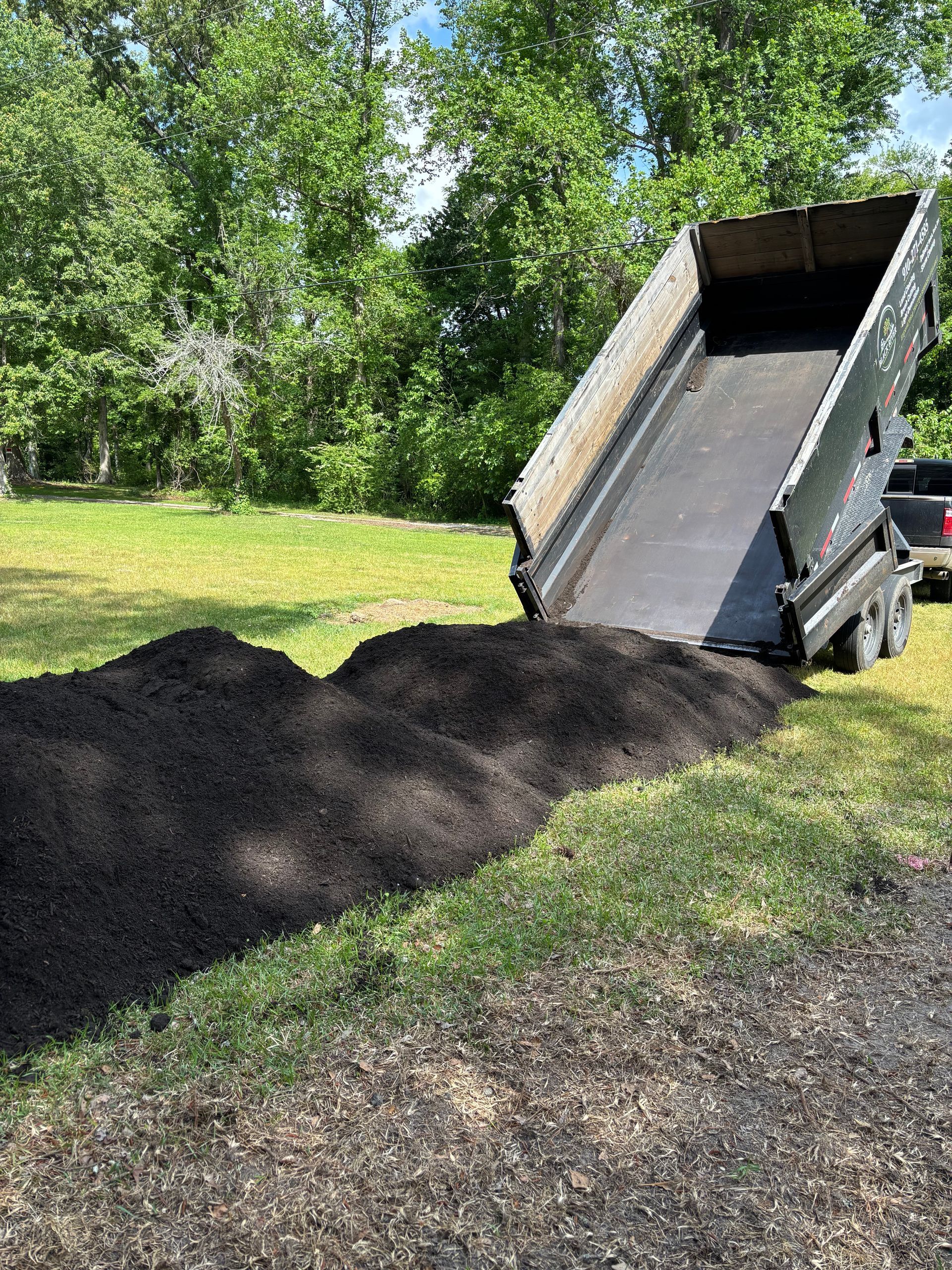 A dumpster filled with dirt is sitting on top of a tarp on the ground.