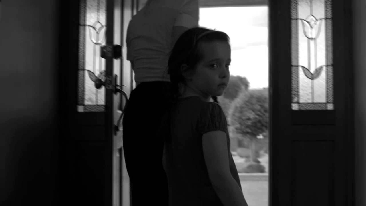Black and white photo of a woman and child standing inside a doorway, looking outside.