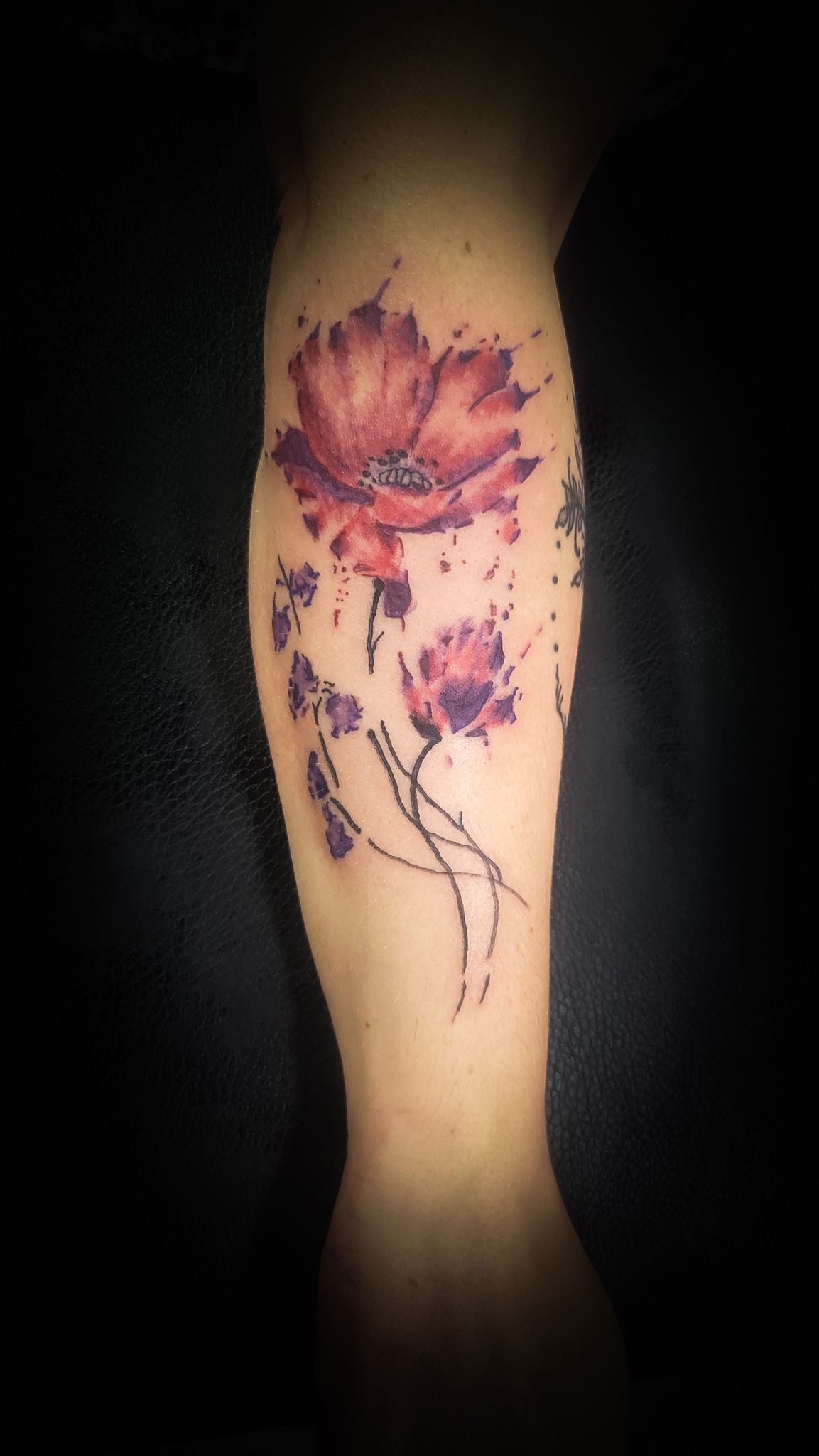 a person has a tattoo of a red flower on their forearm .