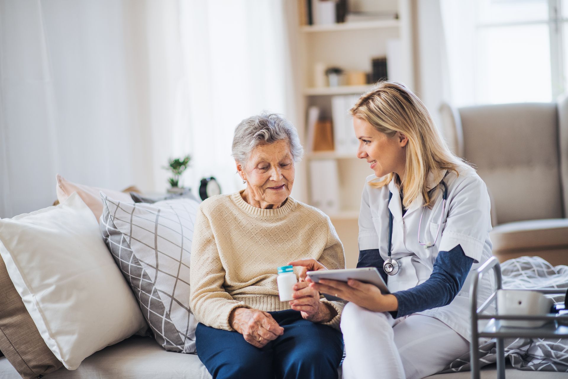 A nurse is talking to an elderly woman while sitting on a couch.